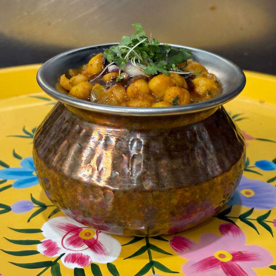 Spiced chickpea curry garnished with fresh herbs and onions, served in a decorative brass bowl on a colorful floral plate.
