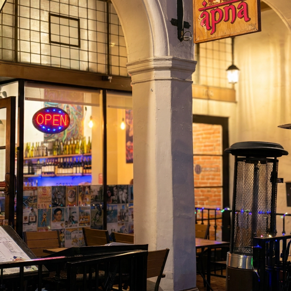 warmly lit restaurant entrance with open doors, outdoor seating, heaters, menu stand, and festive string lights.