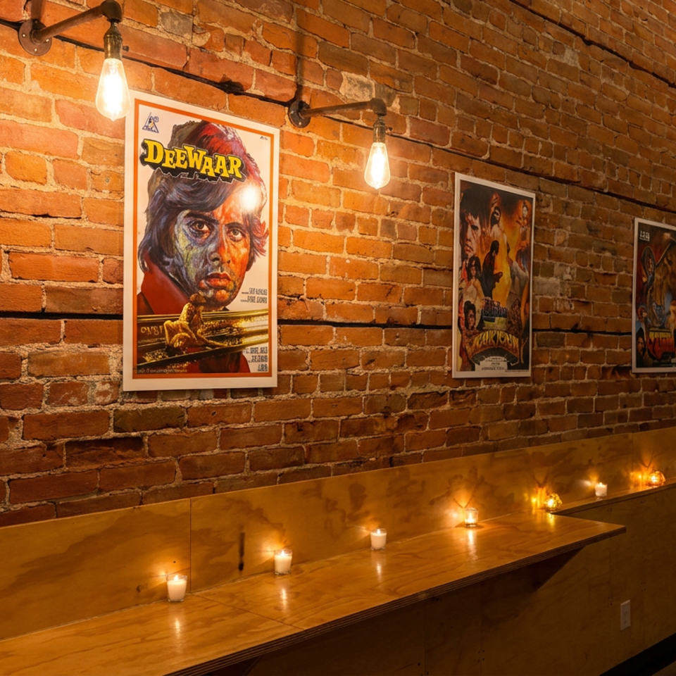 Warm restaurant interior with exposed brick walls, vintage movie posters, hanging bulbs, and candles lining wooden counters.